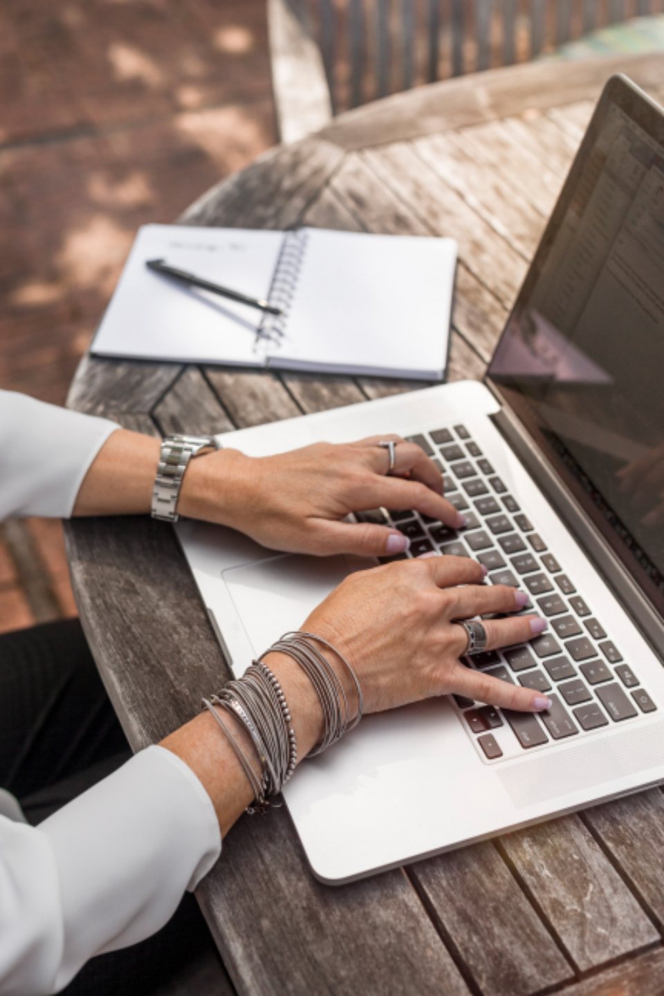 Hands typing on a laptop at an outdoor wooden table