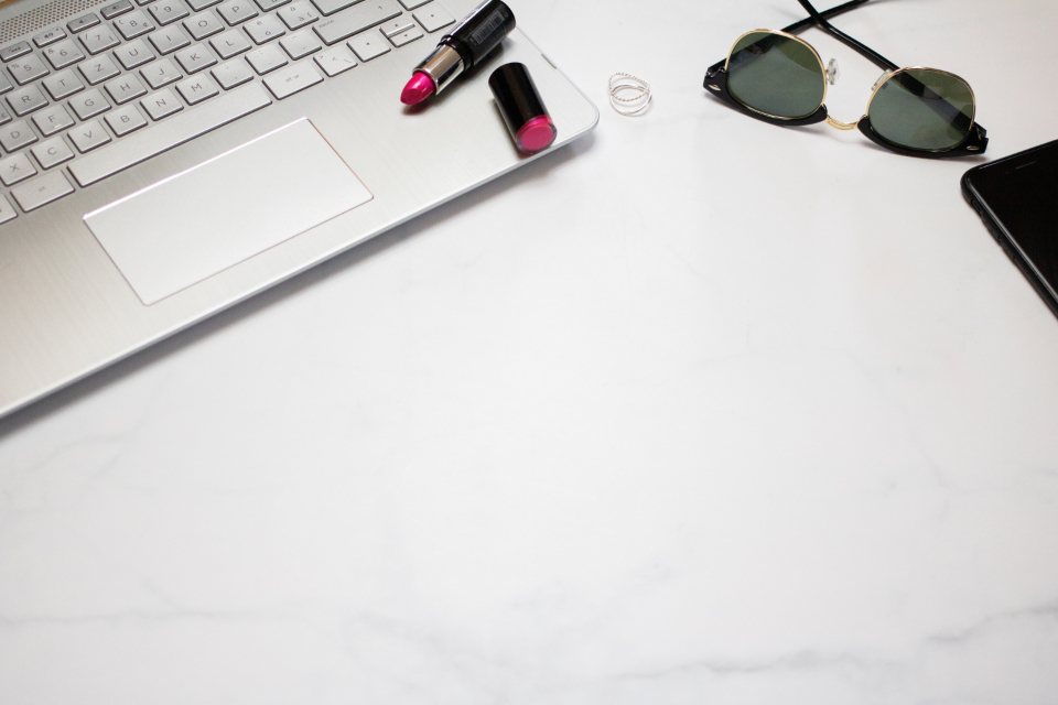 White desk with a laptop, sunglasses and colorful accessories