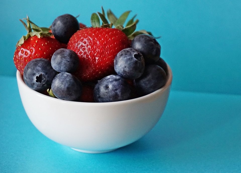 Strawberries and blueberries in a white bowl against a blue background