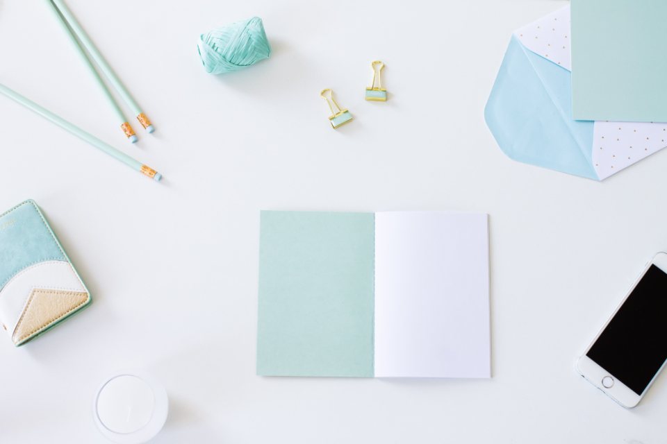 Pastel stationery, pencils and a blank notebook arranged on a white desk