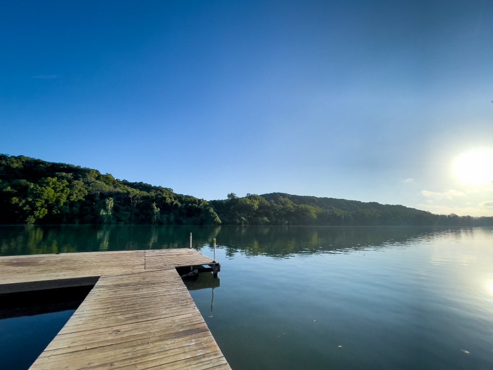 Wooden dock beside a still lake and wooded hills