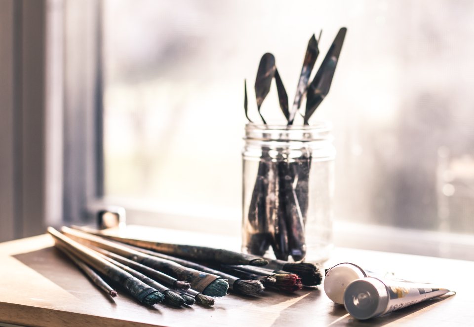 Paintbrushes in a glass jar beside a sunlit studio window
